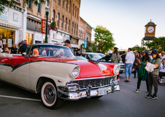 A red and white classic car surrounded by people taking photos